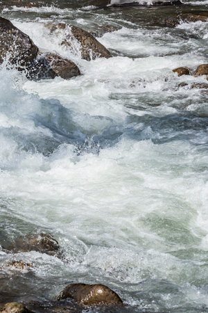 Moving river water. The powerful crash of a river rushing forcefully between rocks. White, foamy waves splash in all directions.の写真素材