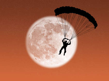 Parachutist in silhouette against a brilliant moonの写真素材