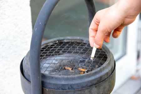 Berlin, Berlin/Germany - 03.09.2019: A hand extinguishing a cigarette in a black standing ashtray with handle and a sieveのeditorial素材