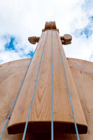 The fingerboard, sides and pegs of a huge violin or violin made of wood photographed from below against the sky.の写真素材