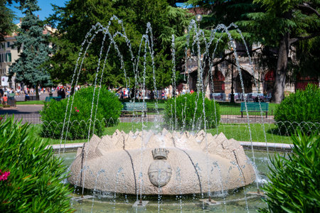 The fountain "Fontana di Piazza BrÃ " in Verona Italy on a busy square with many plants around and bubbling water in the sun.のeditorial素材