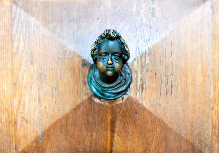 An old door knob in the shape of a metal head, slightly corroded on a brown wooden door with grain and cassettes.の写真素材