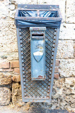 A nostalgic or historic trash can with a garbage bag that is heavily rusted and painted with gray paint, and has an ash shaker on the front of itの写真素材