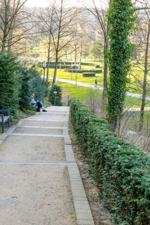 MÃ¼nster, Nordrhein-Westfalen-Germany - 01-04-2021: Path downhill towards a park with a large lawn, lined with hedges and trees and sparse vegetation because it is only spring.のeditorial素材