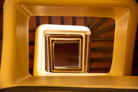 The view into the rectangular central part of a staircase, which is bathed in warm light and where...