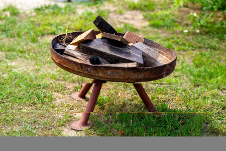A rusty fire bowl filled with various pieces of wood, with three long feet and standing very crooked...