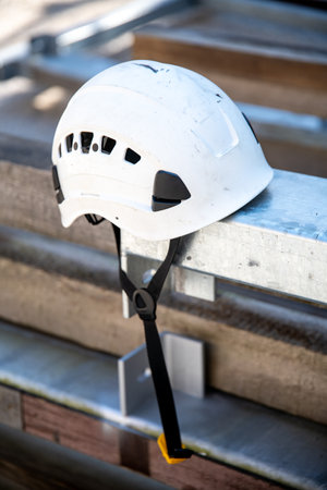 A white safety helmet placed on a metal carrier. The ventilation holes and the chin straps are clearly visible.の写真素材