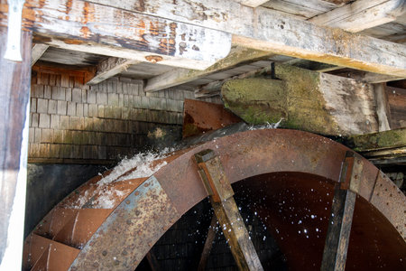 A metal water wheel that is driven by water. The water comes from a wooden frame with an outlet...