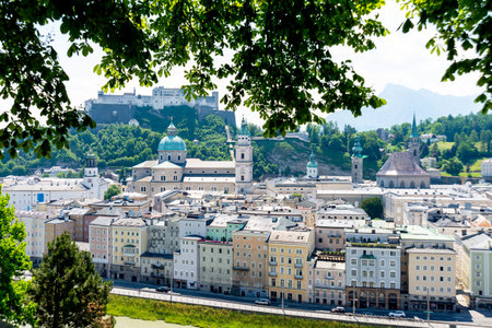 Salzburg, Salzburg - Austria - 06-18-2021: Salzburg's old town and Hohensalzburg Fortress overlook the Salzach River, framed by green foliageのeditorial素材