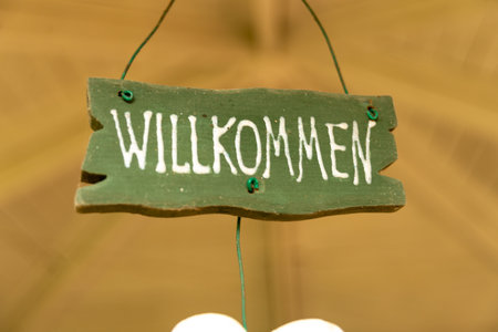 A rustic wooden green sign with "WILLKOMMEN" painted in white, suspended by a wire, symbolizing a German greetingの写真素材