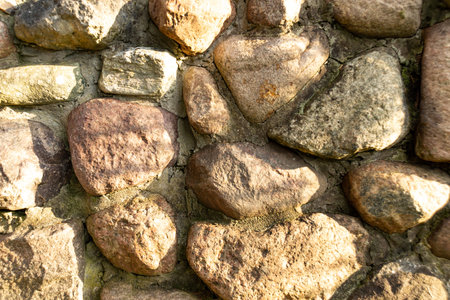 Sunlit cobblestone wall displaying varied textures and hues, with visible mortar joints