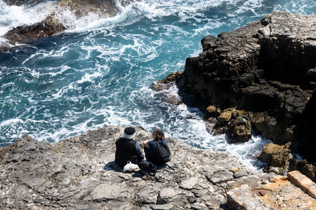 Two people watching waves on rocky Syracuse coastの写真素材
