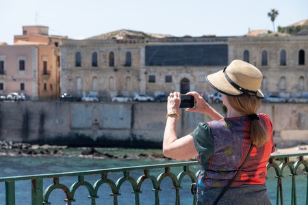 Woman photographing seaside buildings in Syracuse sunlightの写真素材