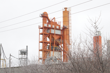 Power line in front of orange mixing block of asphalt plantの写真素材