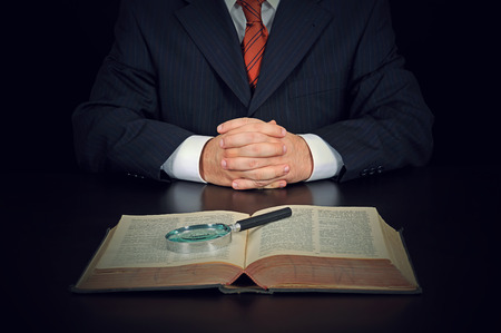 Businessman with old book and magnifying glass on the black backgroundの写真素材