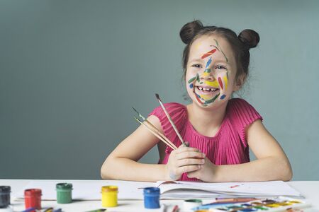 beautiful child with a smeared face in paint with brushes after paintingの写真素材