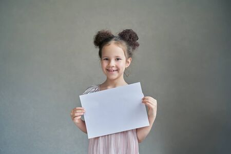 a beautiful funny girl smiles with a white sheet of paper on a gray backgroundの写真素材