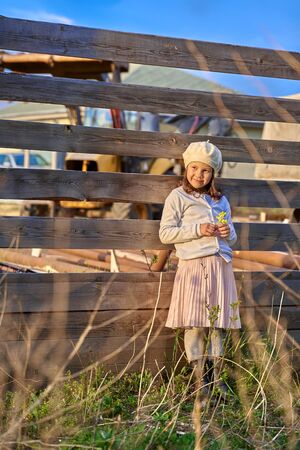 a girl in a white beret stands near a wooden fence in the village and looks at the sunset.の写真素材