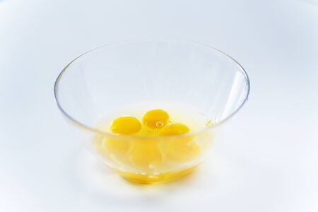 bright broken eggs in a glass plate on a white table.の写真素材
