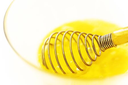 whisk bright eggs in a glass plate on a white table.の写真素材