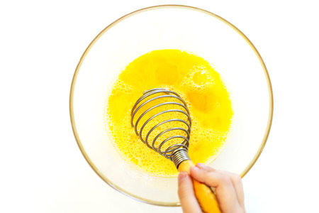 whisk bright eggs in a glass plate on a white table.
