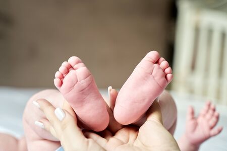 Baby feet in mother hands. Tiny Newborn Baby's feet on female hands closeup. Mom and her Child. Beautiful Soft Conceptual image of Maternityの写真素材