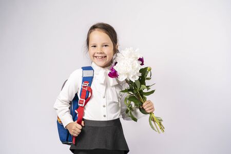first grade school girl in a white shirt holding flowers and a backpack.の写真素材