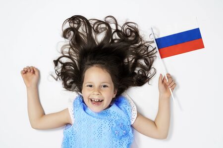 a beautiful girl lies on a white background next to the flag of Russia. the view from the top.の写真素材