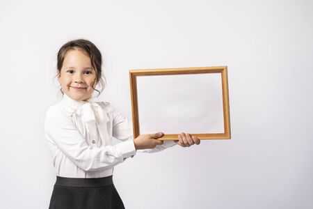 a beautiful first grade school girl in a white shirt holds a white sheet for the inscriptionの写真素材