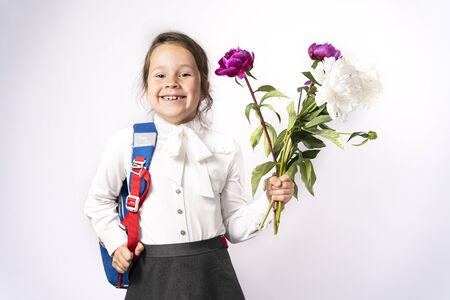 first grade school girl in a white shirt holding flowers and a backpack.の写真素材