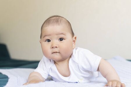 A newborn Asian cute boy in a white bodysuit lies on his tummy and looks into the frame.の写真素材