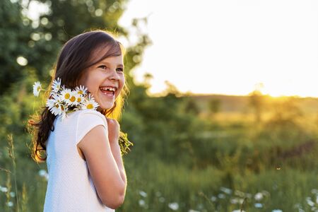 a beautiful girl with daisies smiles against the background of the sunset.の写真素材