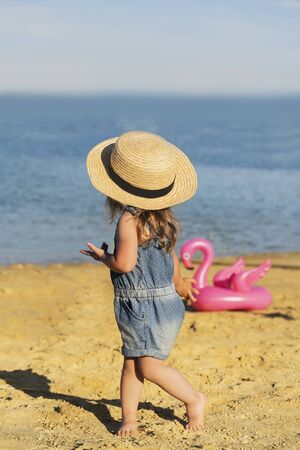 beautiful little girl in a straw hat on a sandy beach against the sea.の写真素材
