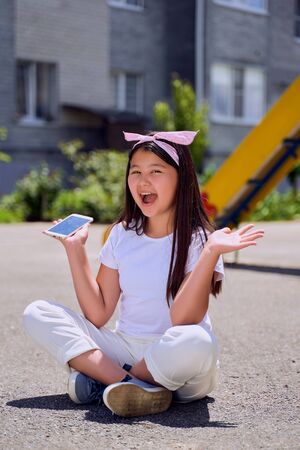 beautiful little Asian girl with phone on the street is surprised.の写真素材