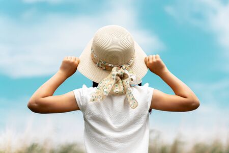 a girl in a straw hat against the blue sky. rear view.の写真素材