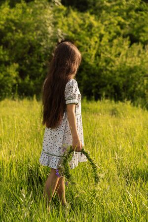 a girl holds a wreath of flowers. rear view. sunset.の写真素材