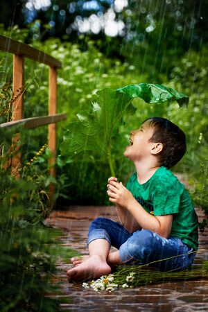 a little boy is sitting in the rain and is covered with burdockの写真素材