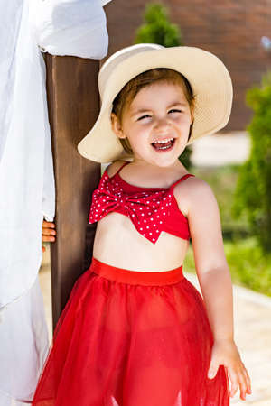 a little girl in a hat and a red skirt on the beach laughs.の写真素材