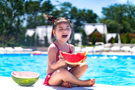 a girl in a swimsuit stands with a watermelon on the beach.の写真素材