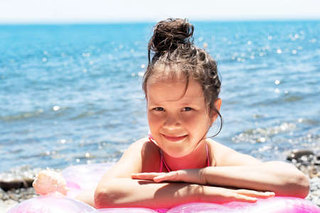 a beautiful little girl is lying on a bathing mattress near the sea.の写真素材