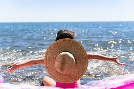 beautiful little girl by the sea with a hat looks at the sea and hands away.の写真素材