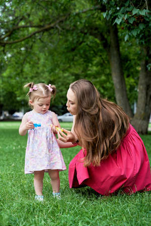 a little girl with her mother playing with soap bubbles on a green lawn.の写真素材