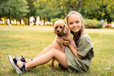 a girl is sitting on a green lawn with a poodle dogの写真素材