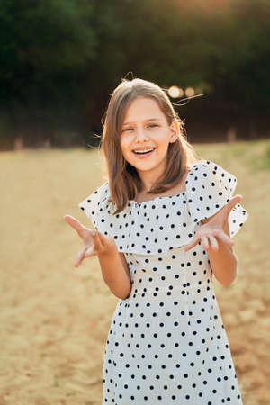 a little girl on the beach in a polka dot dress laughs and puts her hands out to the sideの写真素材