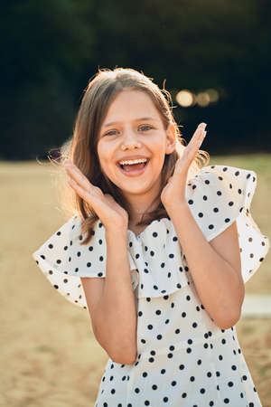 a little girl on the beach in a polka dot dress laughs and puts her hands out to the sideの写真素材