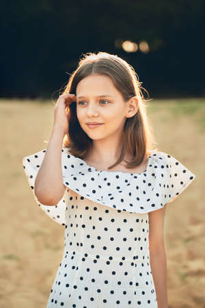 a girl on the beach in a polka dot dress looks into the distance and straightens her hairの写真素材