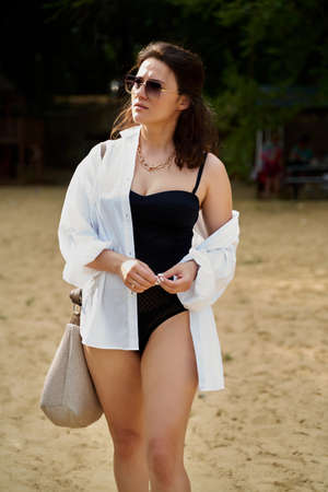 cute fashion girl on the beach in a black swimsuit, white shirt and glasses.の写真素材