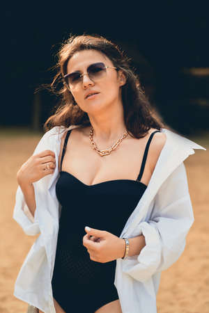 cute fashion girl on the beach in a black swimsuit, white shirt and glasses.の写真素材