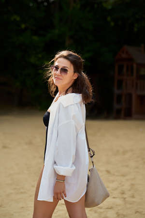 cute fashion girl on the beach in a black swimsuit, white shirt and glasses.の写真素材