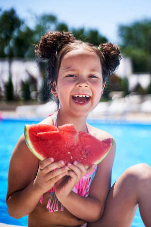 a girl in a swimsuit stands with a watermelon on the beachの写真素材